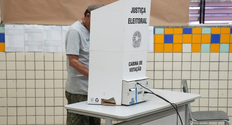 Um eleitor realiza a votação em uma urna eletrônica instalada sobre uma mesa, em uma seção eleit...